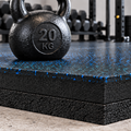 Black rubber gym flooring with blue speckles, shown in a gym setting with a 20 kg kettlebell on top and weight racks in the background.