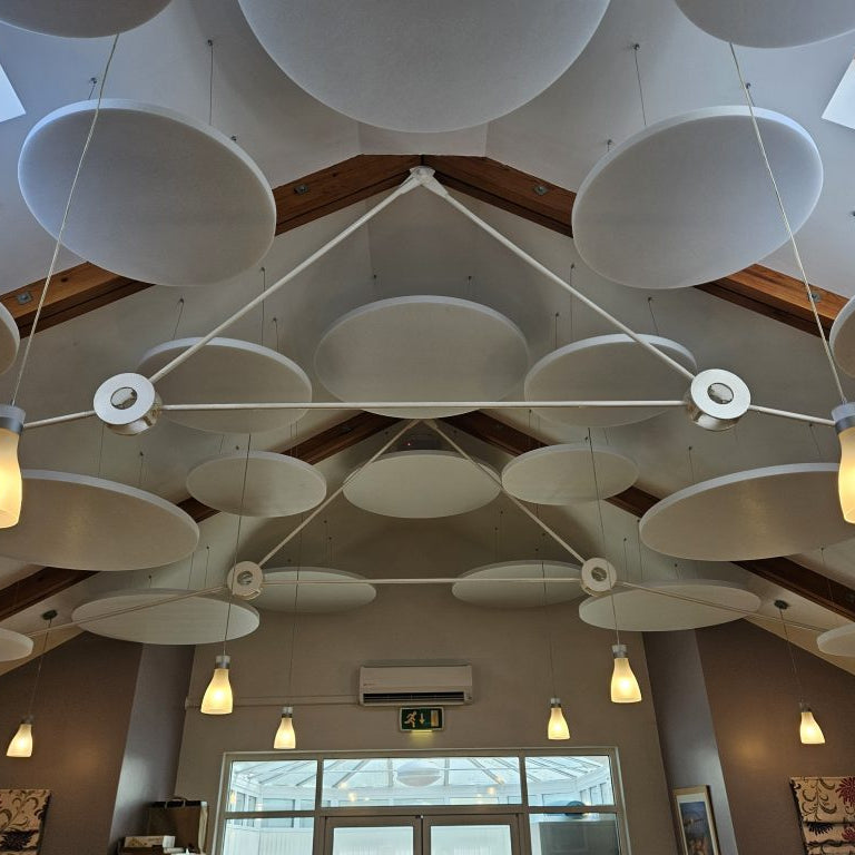 Ceiling with modern white acoustic panels and pendant lights in a room with large windows.