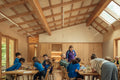 A ambient room full of children in a bright, wood-paneled classroom with a high slanted ceiling and skylights.