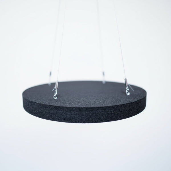 A black acoustic ceiling panel hanging by a metal wires and clips, against a background of a studio